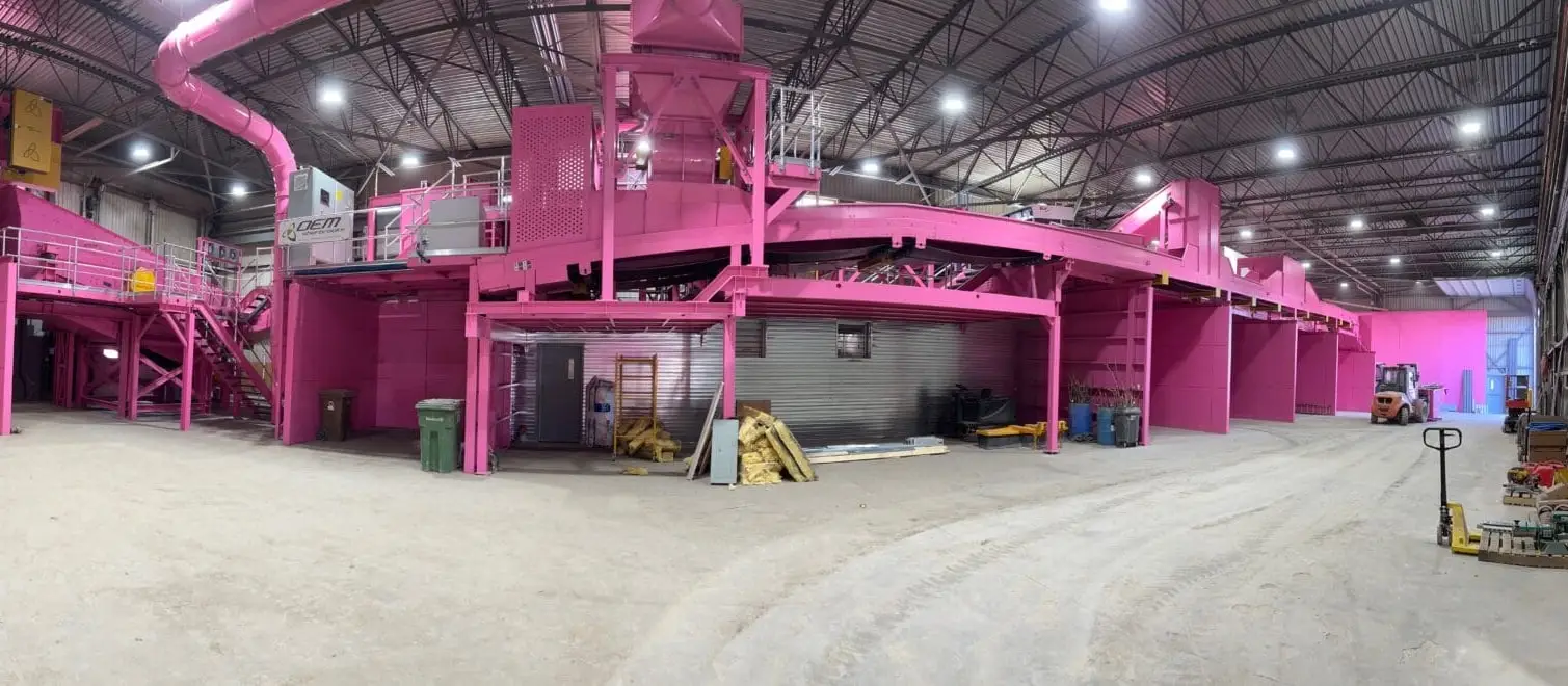 Vue d'ensemble de la halle de tri : la ligne de convoyeurs peinte en magenta sur toute sa longueur, et le plancher de déchargement au premier plan